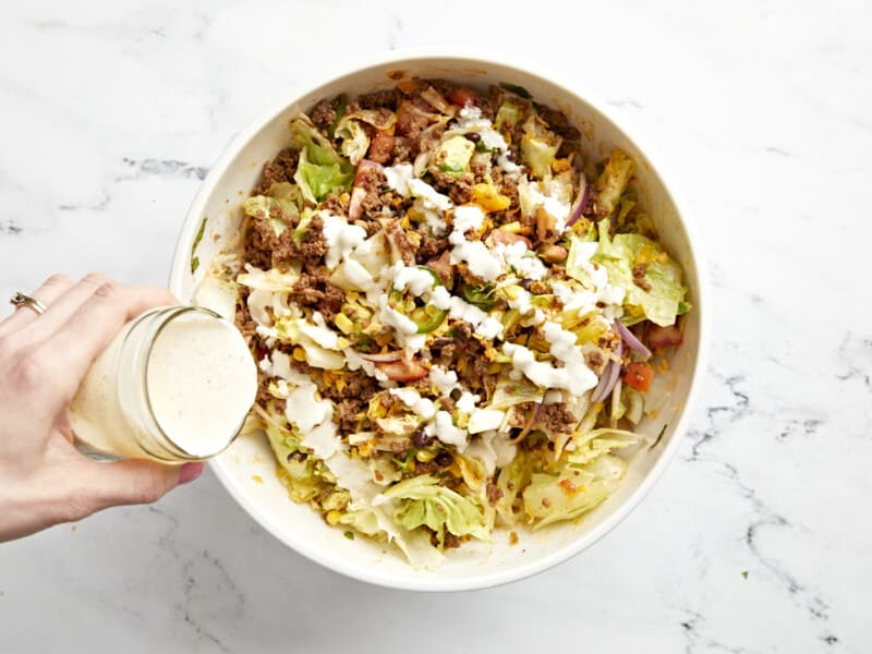 drizzling dressing over taco salad in a white bowl.
