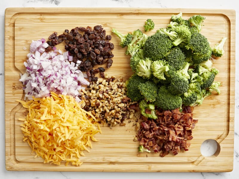 overhead view of ingredients for broccoli salad on a wooden cutting board.