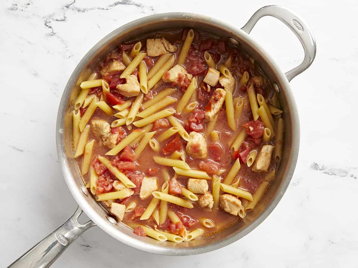 Uncooked pasta in a pan with chicken and tomatoes. 