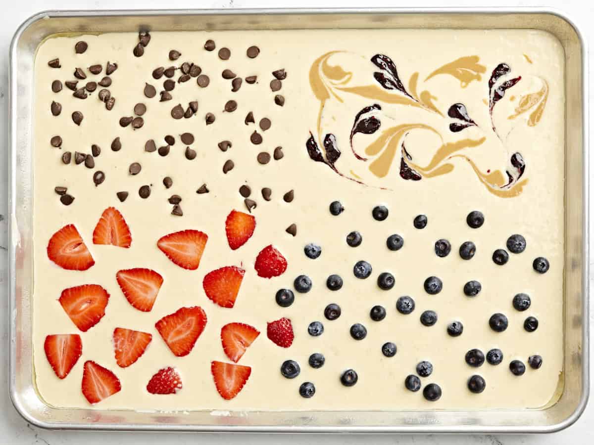 Pancake batter poured from a sheet pan with fruit on top and poured onto a sheet pan.