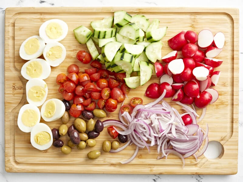 overhead view of prepped ingredients for nicoise salad on a cutting board.
