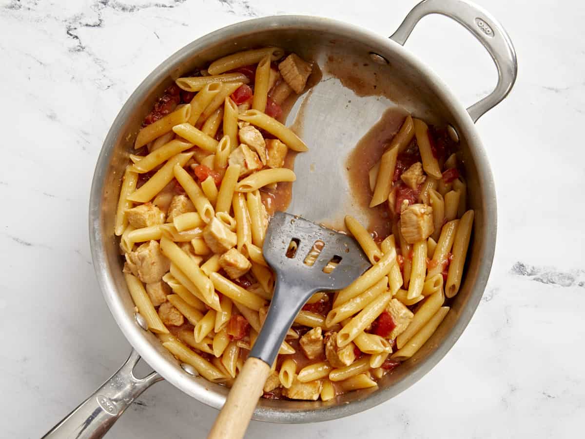Cooked pasta in the skillet, a spatula pulling the pasta to the side to show the thickened sauce.