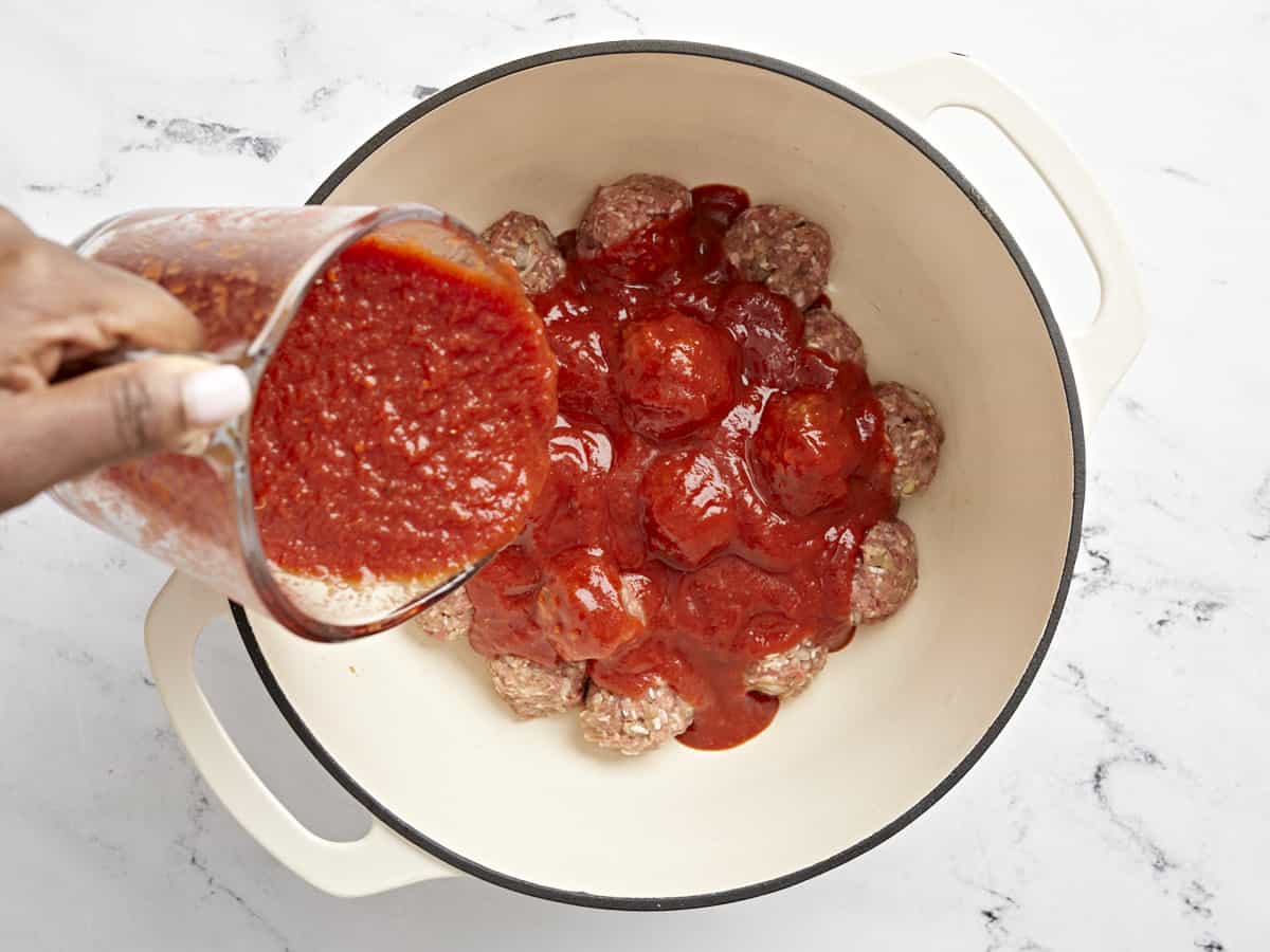 Tomato sauce being poured over meatballs in the dutch oven.