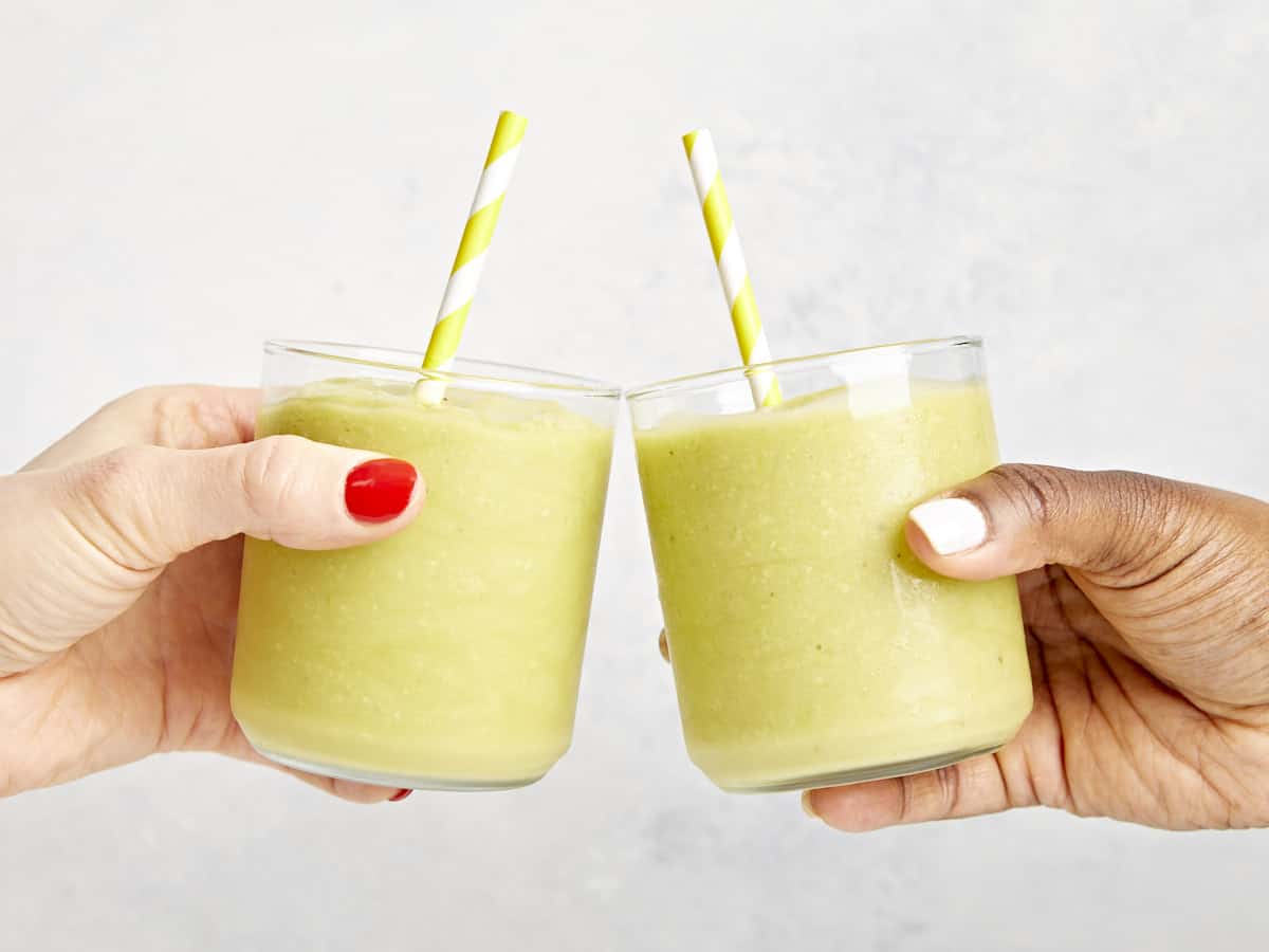 two hands clinking avocado smoothies together.