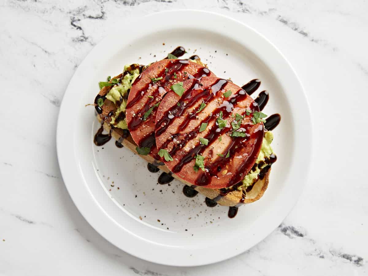 Avocado toast with sliced tomatoes and balsamic glaze drizzled on top.