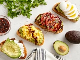 Overhead view of avocado toast made 4 different ways with parsley, avocado, and a napkin on the side.