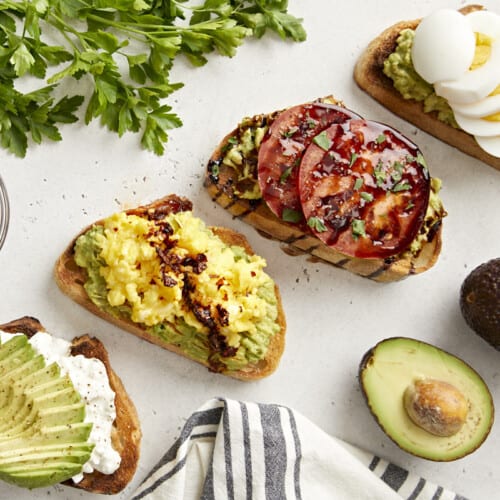 Overhead view of avocado toast made 4 different ways with parsley, avocado, and a napkin on the side.