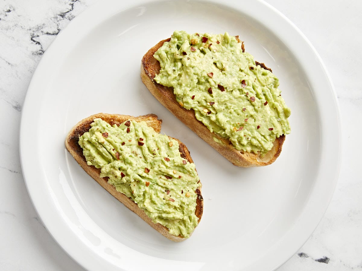 Overhead view of 2 pieces of plain avocado toast on a white plate.