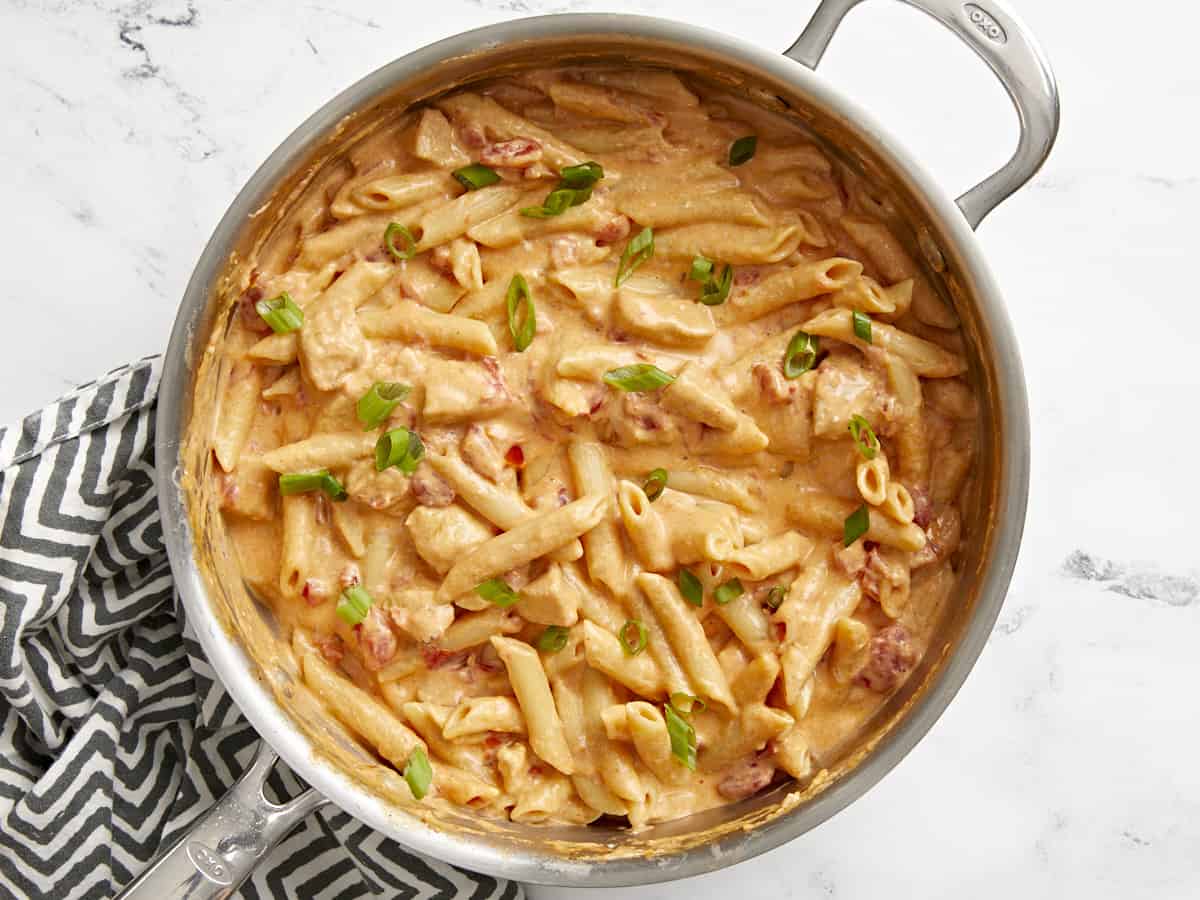 Top view of a pan full of buffalo chicken noodles with a striped napkin on the side. 