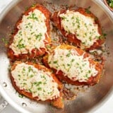 overhead view of 4 fried chicken breasts topped with marinara sauce, melted cheese, and parsley in a stainless skillet.