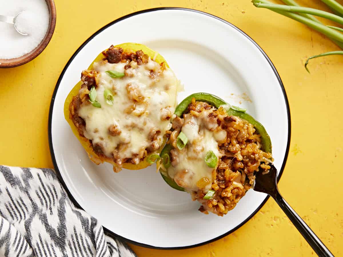 Overhead view of two stuffed bell peppers on a plate with a fork digging into one.