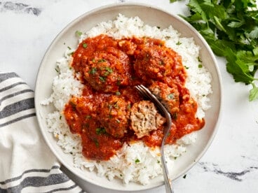 Overhead view of porcupine meatballs on a serving plate with white rice and a fork cutting a meatball in half.