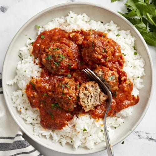 Top view of porcupine meatballs on a serving plate with white rice and a fork cutting a meatball in half.