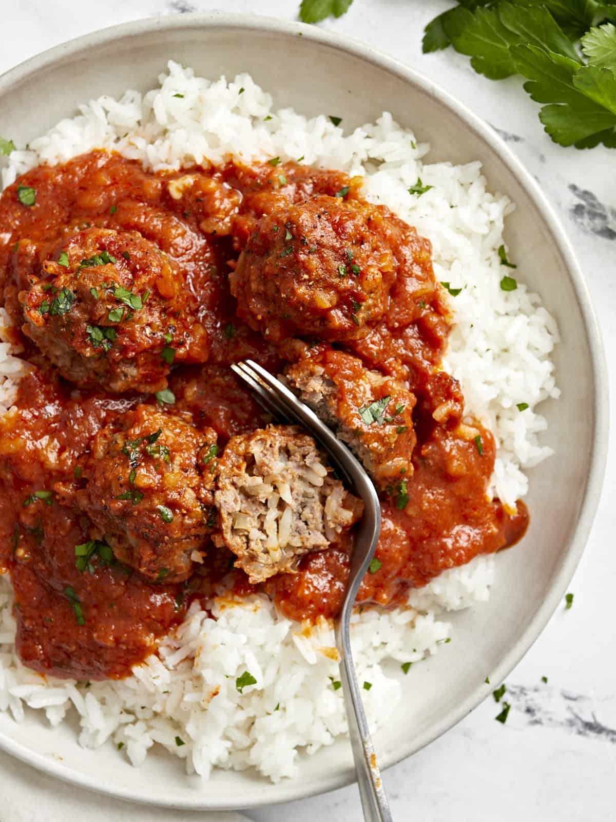 Overhead view of porcupine meatballs on a serving plate with white rice and a fork cutting a meatball in half.