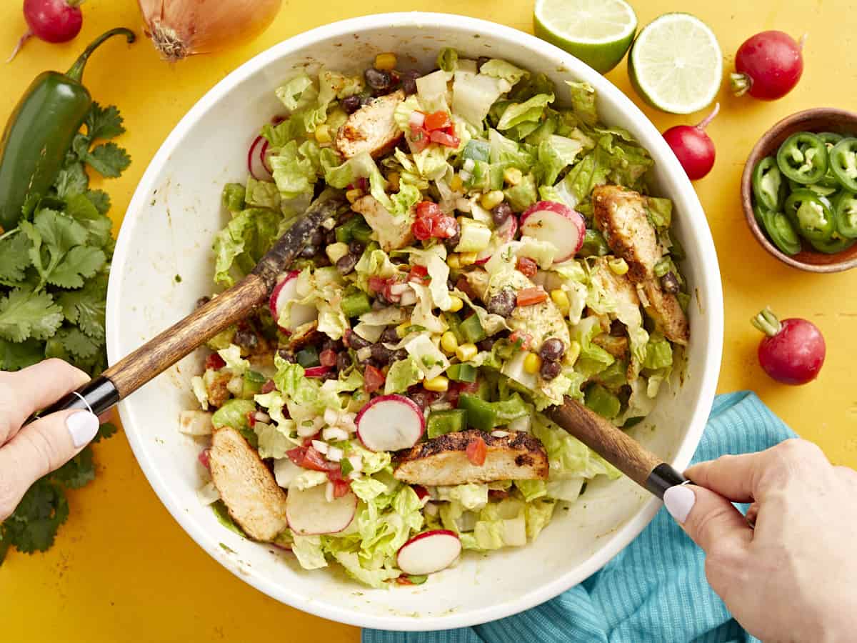 tossing santa fe salad in a large white bowl with wooden spoons.