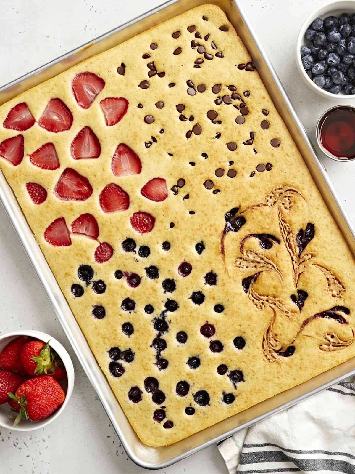 Top view of sheet pan pancakes with fresh fruit and maple syrup on the side.