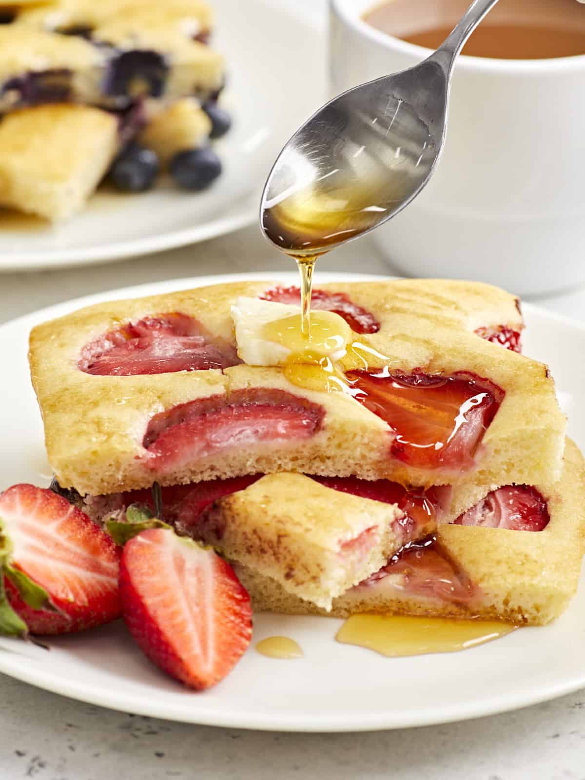 Close-up of strawberry sheet pan pancakes on a serving plate with maple syrup drizzled on top.