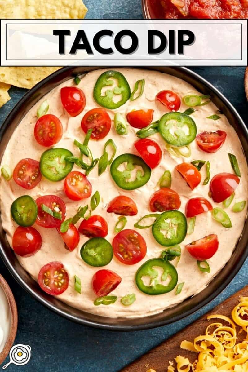 Overhead view of a serving bowl full of taco dip, topped with cherry tomatoes and jalapenos with title text at the top.