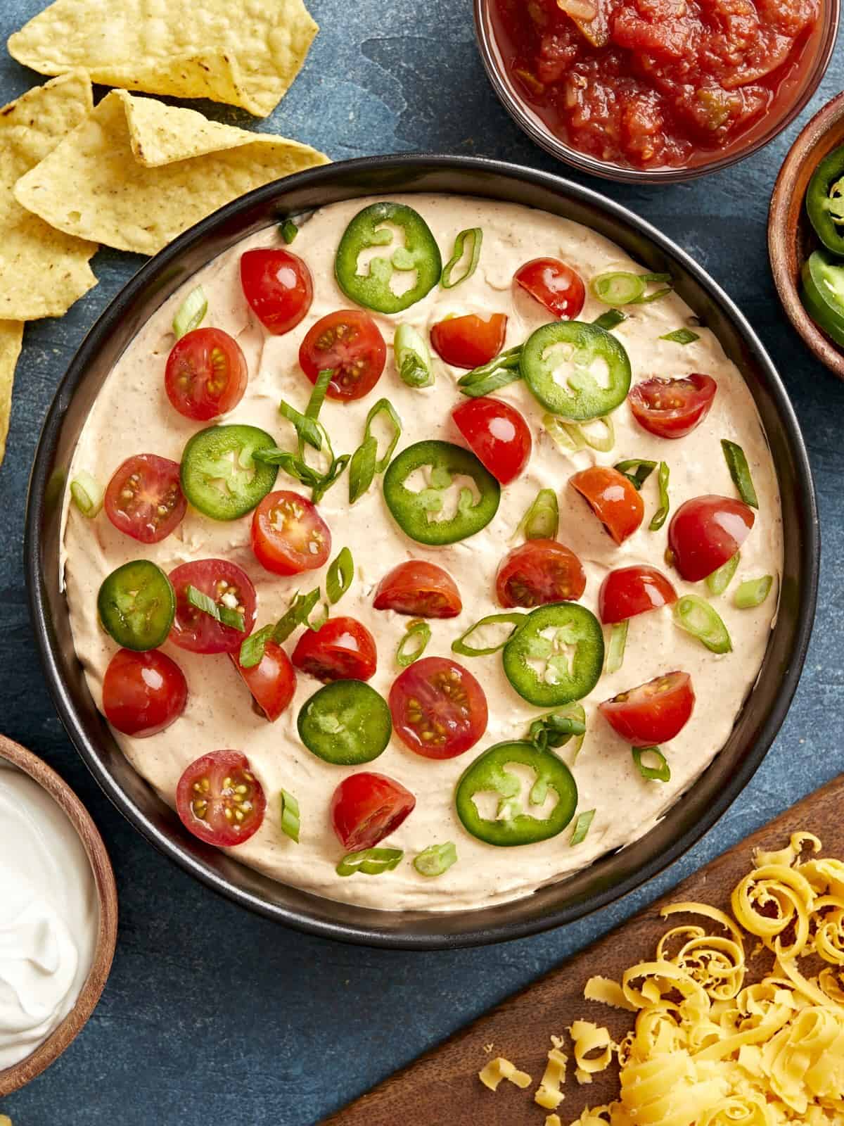 Overhead view of a serving bowl full of taco dip, topped with cherry tomatoes and jalapenos and chips served on the side.