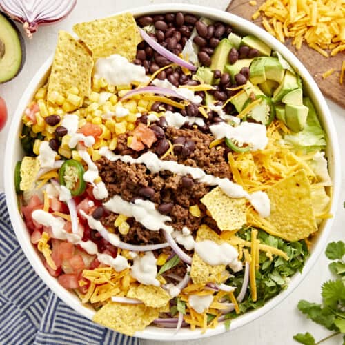 Top view of taco salad with creamy white dressing and corn chips in a white bowl.