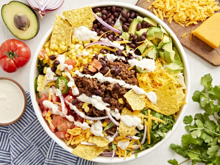 overhead view of taco salad with creamy white dressing and corn chips in a white bowl.