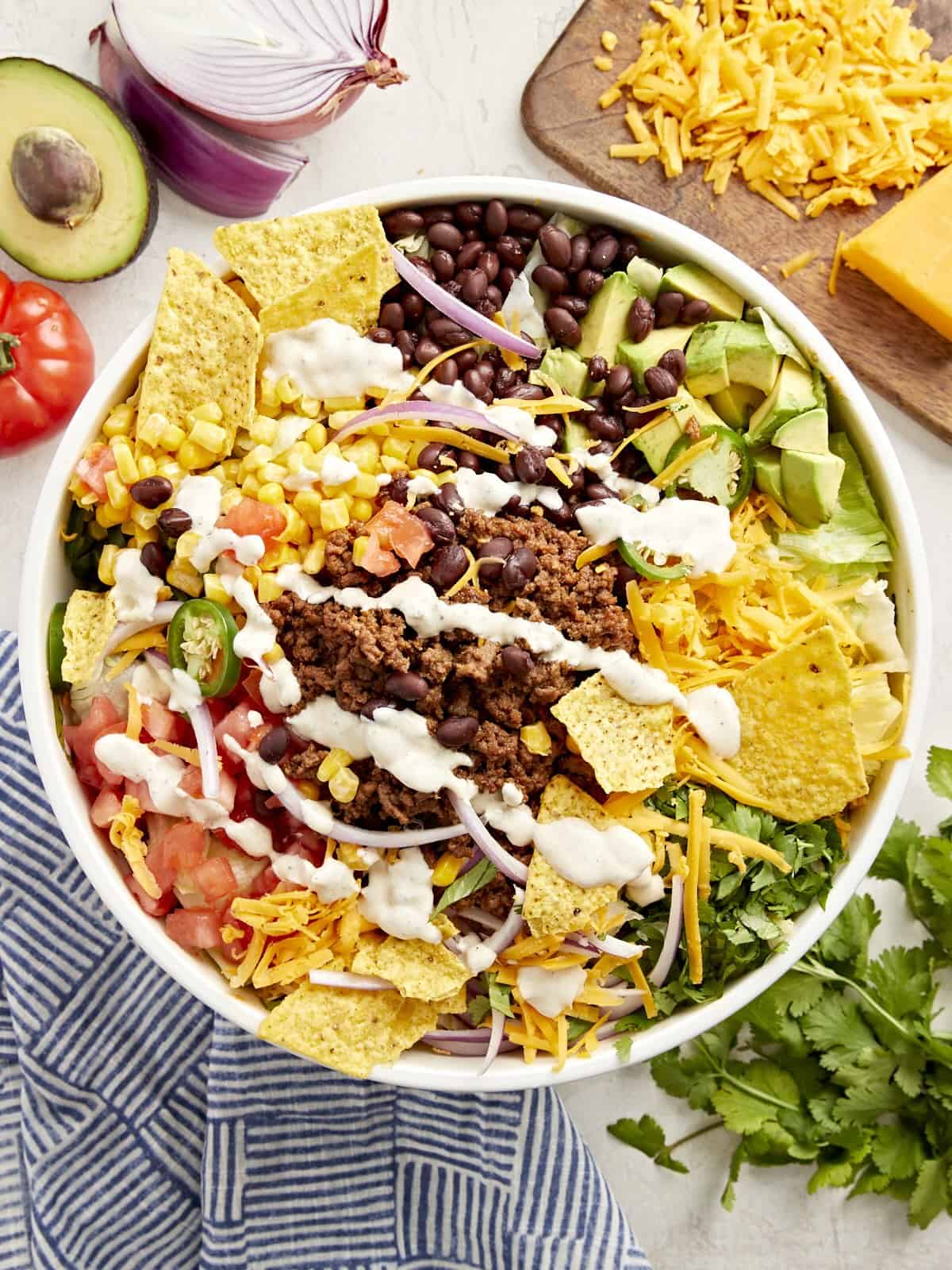 Top view of taco salad with creamy white dressing and corn chips in a white bowl.