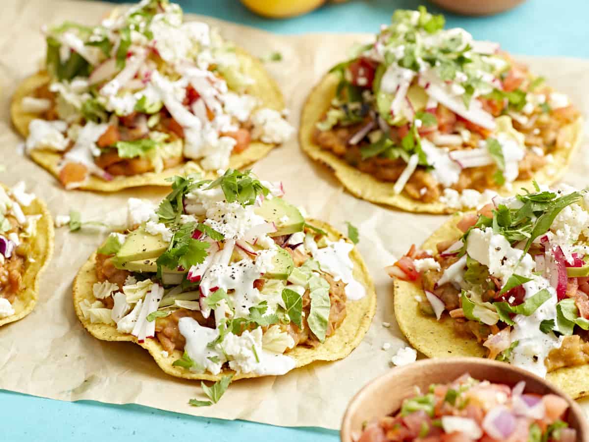 side view of tostadas on a piece of parchment paper on a blue table.