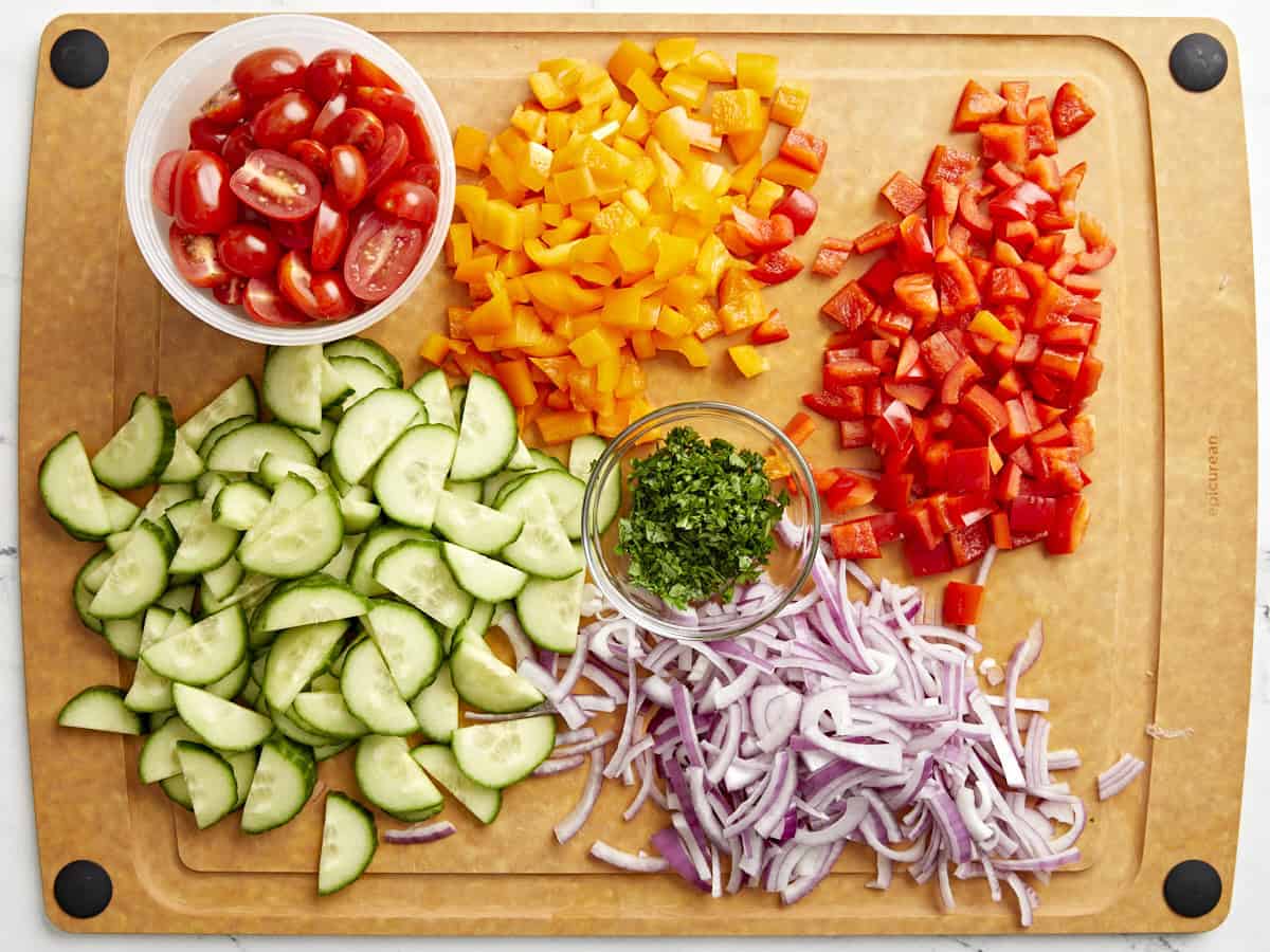 Chopped pasta salad vegetable ingredients on a cutting board.