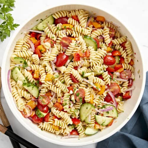 Overhead view of pasta salad in a large white serving bowl with wood serving utensils on the side.