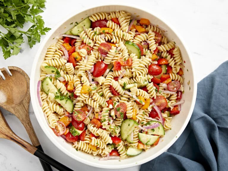 Overhead view of pasta salad in a large white serving bowl with wood serving utensils on the side.