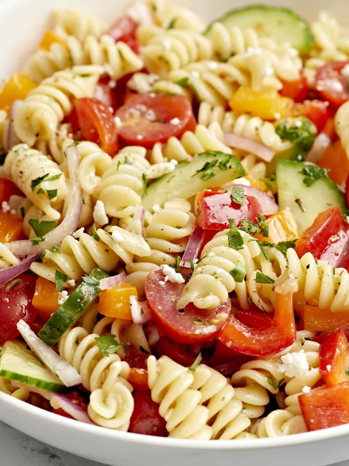 Close up view of pasta salad in a white serving bowl.