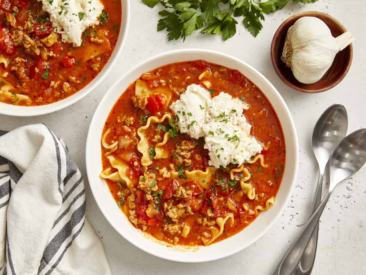 Bowl of lasagna soup with cheese toppings with spoons and a dishcloth.