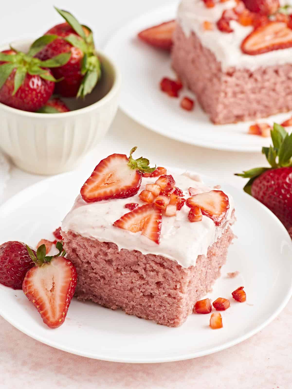 Vue latérale d'une part de gâteau aux fraises sur une petite assiette blanche avec des fraises fraîches à côté.