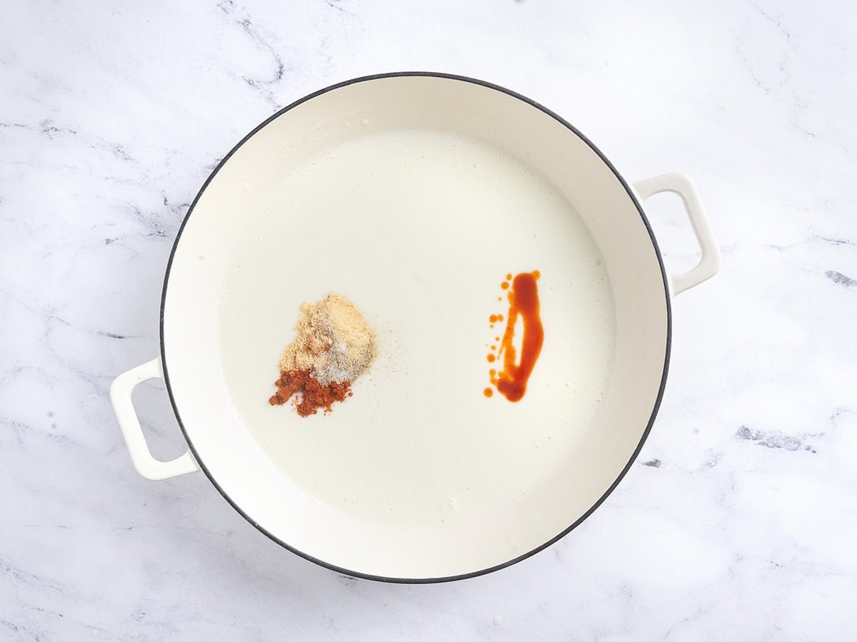 Seasonings and hot sauce added to a creamy sauce in a skillet.