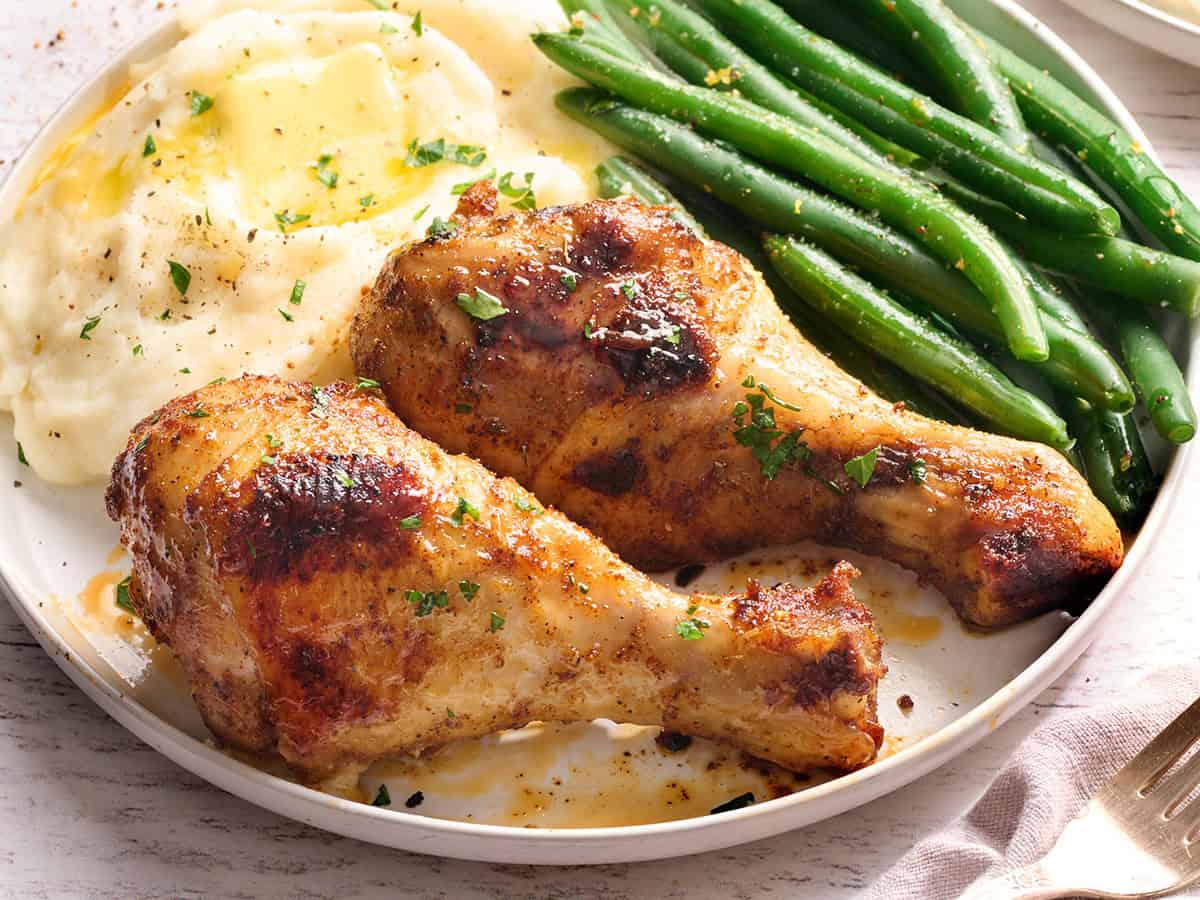 Baked chicken drumsticks on a plate with green beans and mashed potatoes.