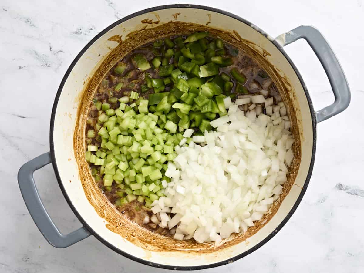 Diced bell pepper, onion, and celery in a dark brown roux in a pot.