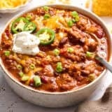 Front side view of a bowl of homemade chili with sour cream and sliced jalapenos.
