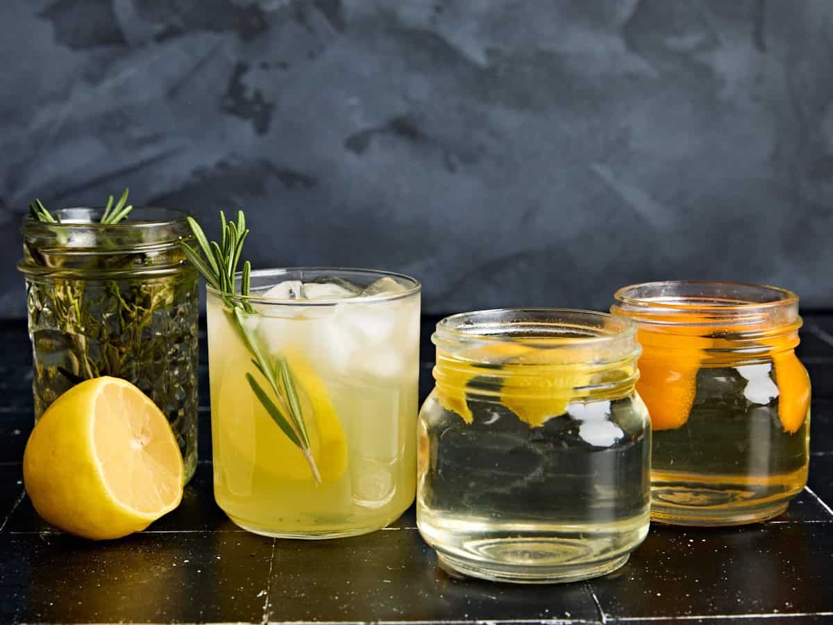Side view of three jars of homemade simple syrup and a cocktail in a glass.