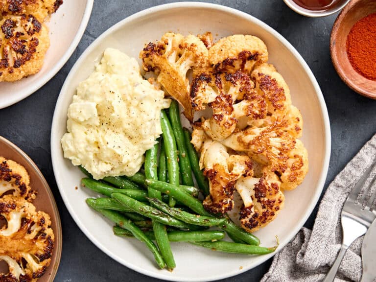 Overhead view of cauliflower steaks on a plate with mashed potatoes and green beans.