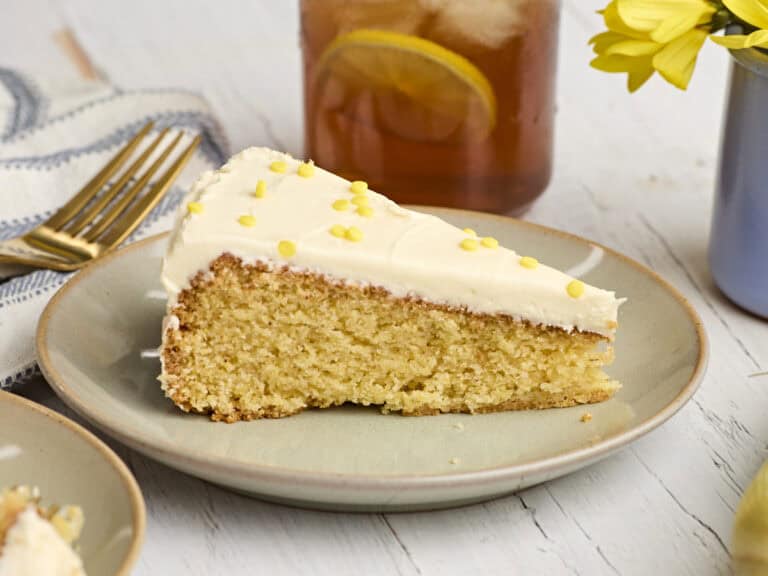 Side view of a cornbread cake, topped with honey buttercream frosting on a plate.