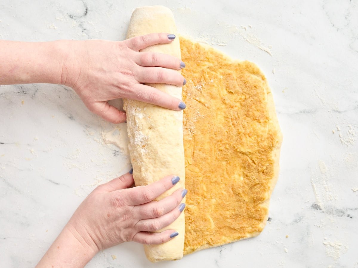 Hands rolling dough to create orange rolls.