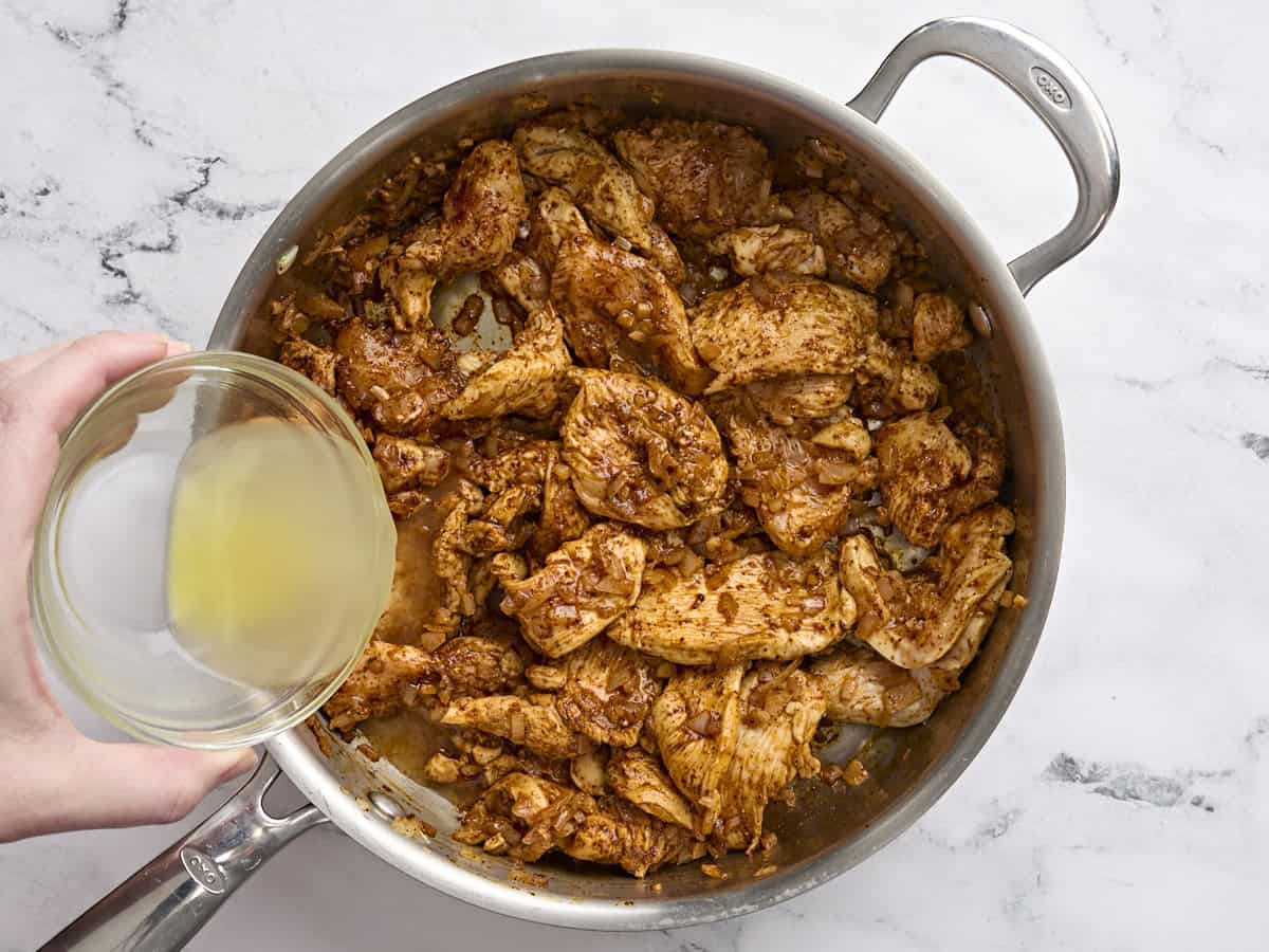 Broth being poured into cooked chicken in a saute pan to make baked chicken chimichnagas.