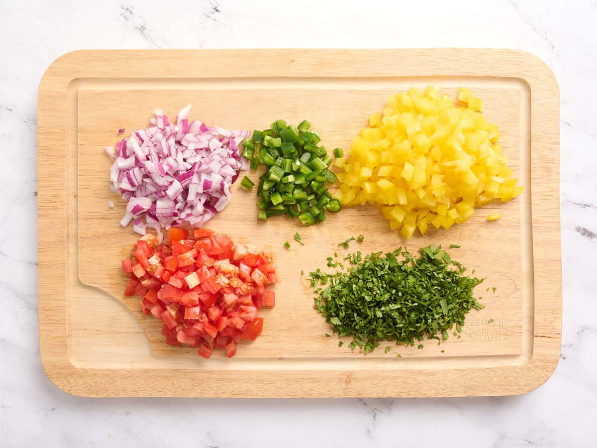 Diced onion, tomato, bell pepper, jalapeno, and cilnatro on a wooden cutting board.