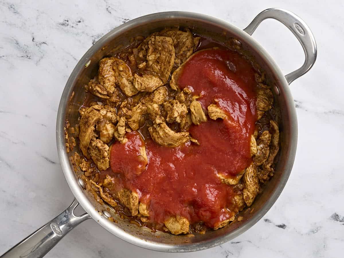 Canned tomato sauce added to a skillet with the filling for baked chicken chimichangas.