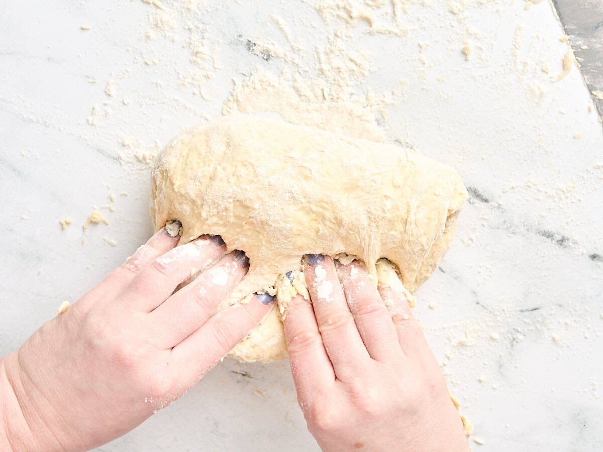 The homemade dough for orange rolls being folded over by two hands.