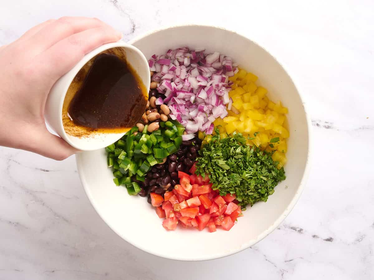 Cowboy caviar ingredients in a bowl with the dressing being poured over top.