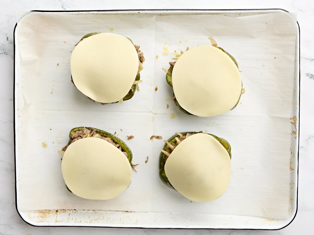 Philly cheesesteak stuffed peppers topped with a slice of provolone cheese on a baking sheet.