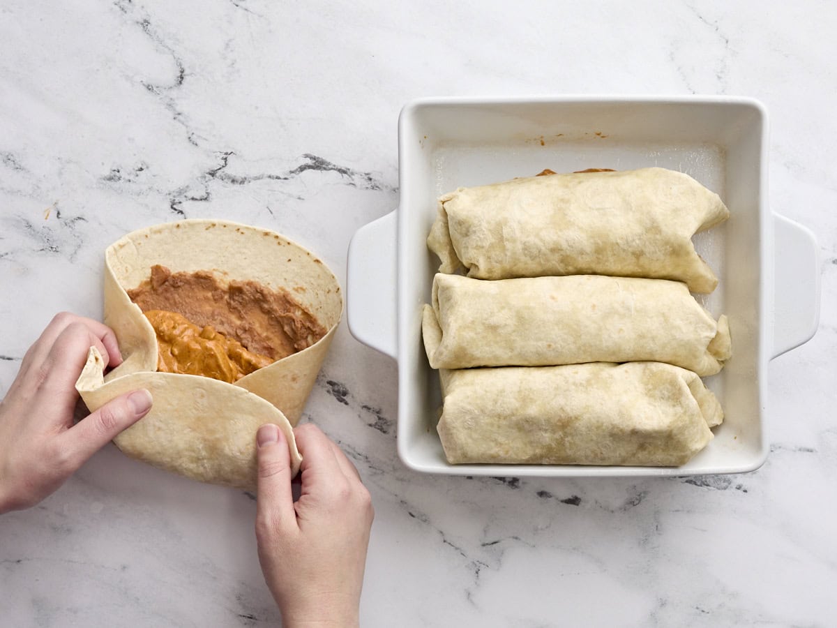A hand folding homemade chicken chimichangas.