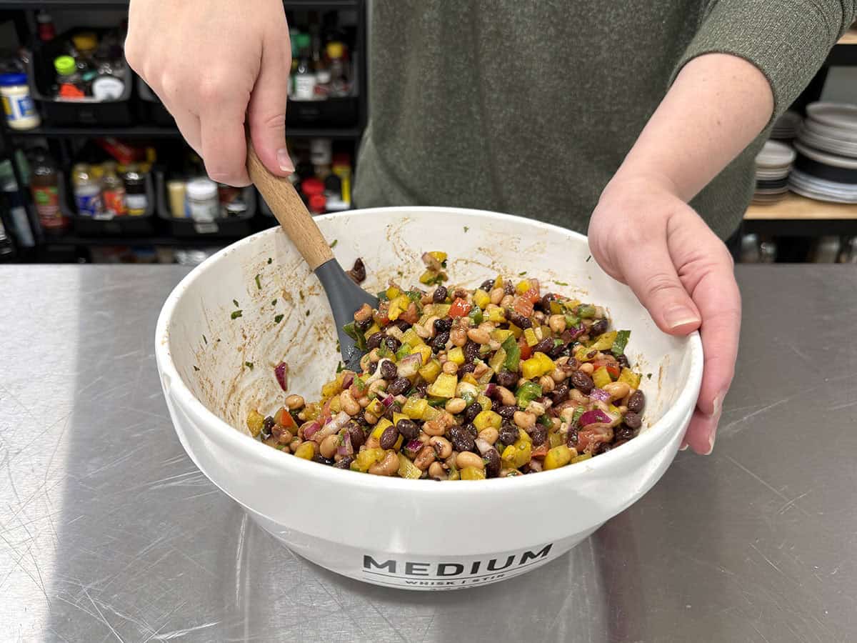 Front view of hands holding a bowl of cowboy caviar and mixing it with a spoon.