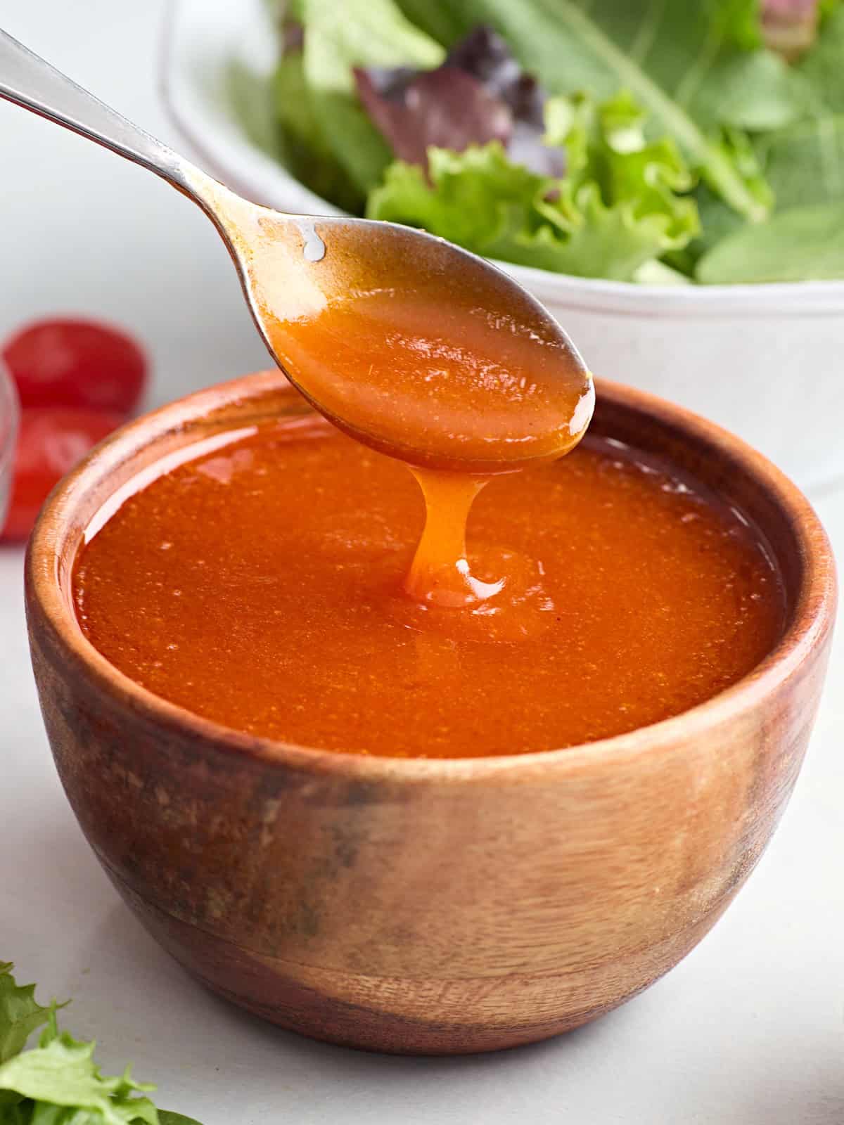 Side view of a bowl of french dressing, with a spoon taking some.